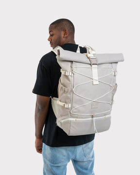Mann mit schwarzem T-Shirt und Jeans trägt beigefarbenen Johnny Urban Reiserucksack 'Allen Large Travel' mit gerolltem Verschluss und elastischen Schnüren