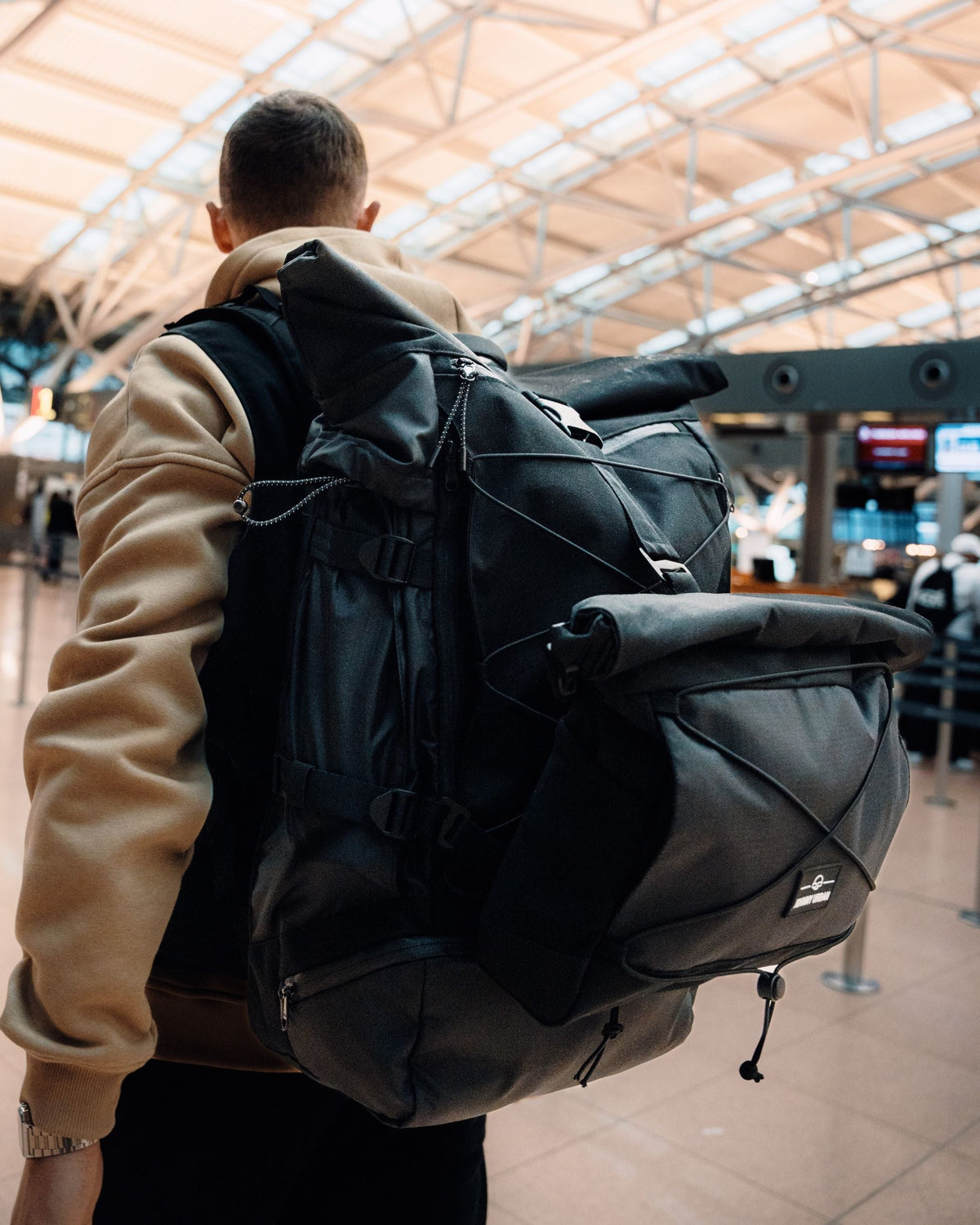 Mann mit beigefarbenem Pullover trägt schwarzen Reiserucksack 'Allen XL Travel' am Flughafen