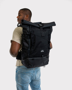 Mann mit beigem T-Shirt trägt schwarzen Reiserucksack 'Allen XL Travel' von Johnny Urban mit Rollverschluss und Fronttasche