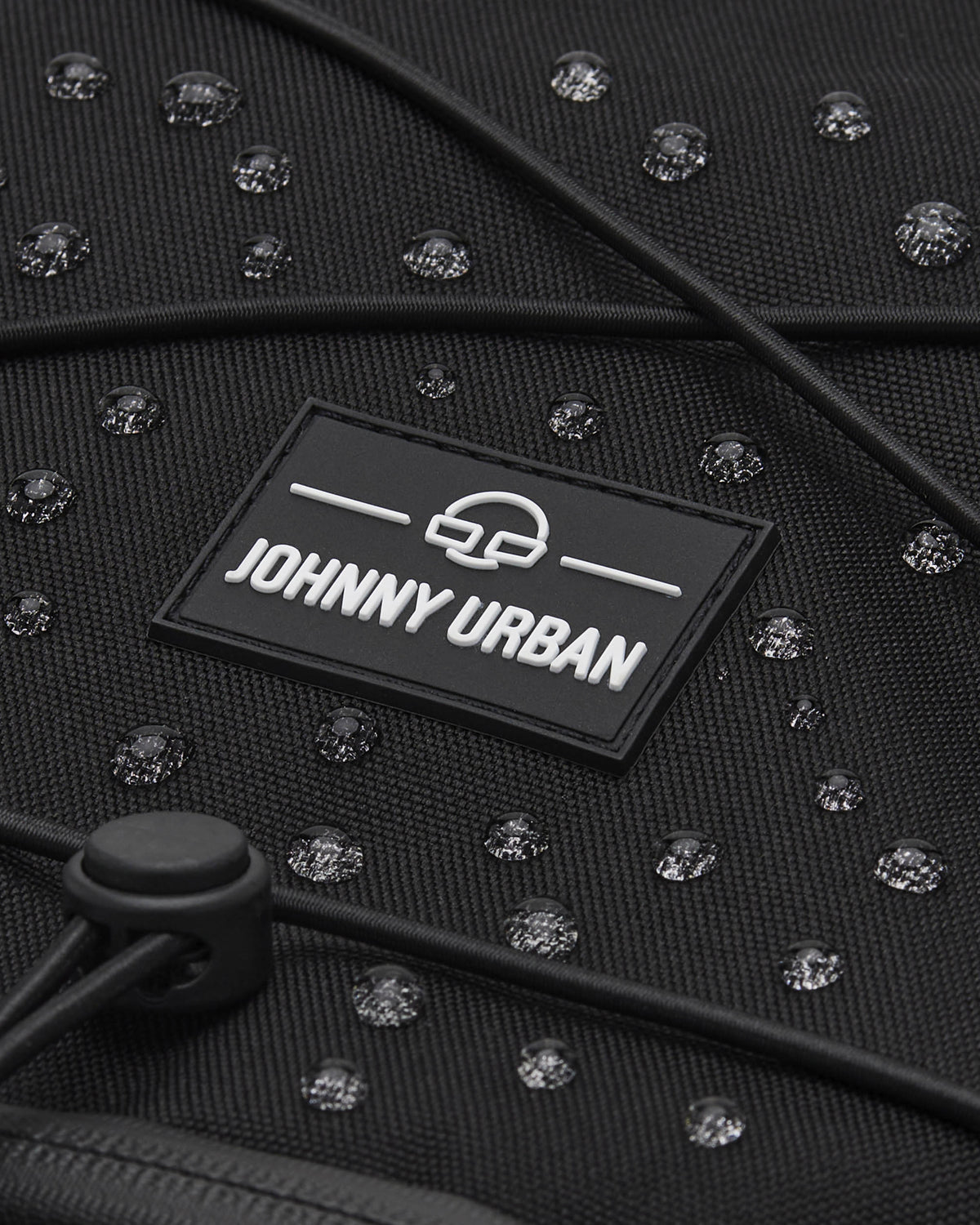 Nahe Aufnahme des schwarzen, wasserabweisenden Reiserucksacks Allen Large Travel von Johnny Urban mit sichtbaren Wassertropfen