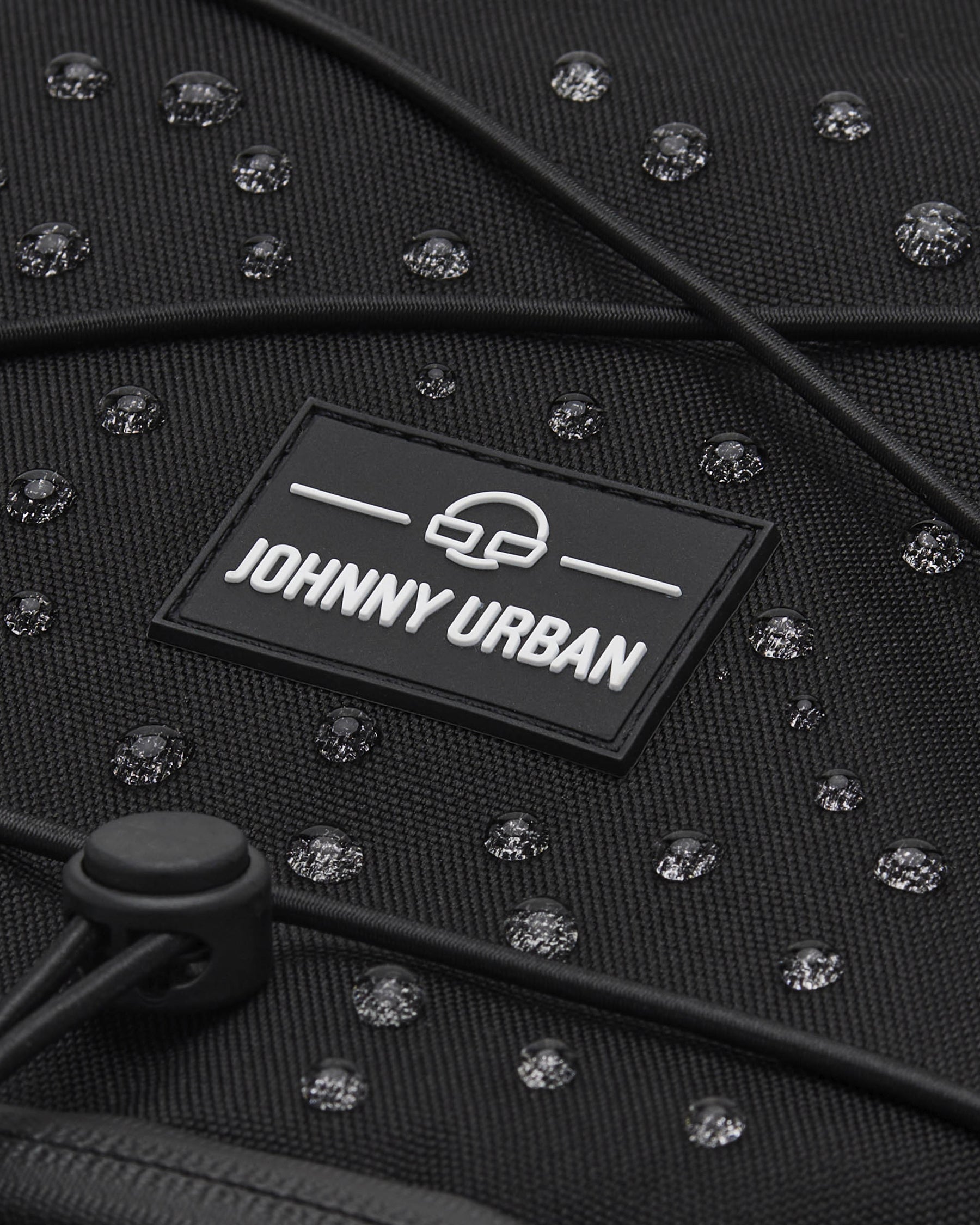 Nahaufnahme des schwarzen wasserabweisenden Reiserucksacks 'Allen XL Travel' mit JOHNNY URBAN Logo und Wassertropfen
