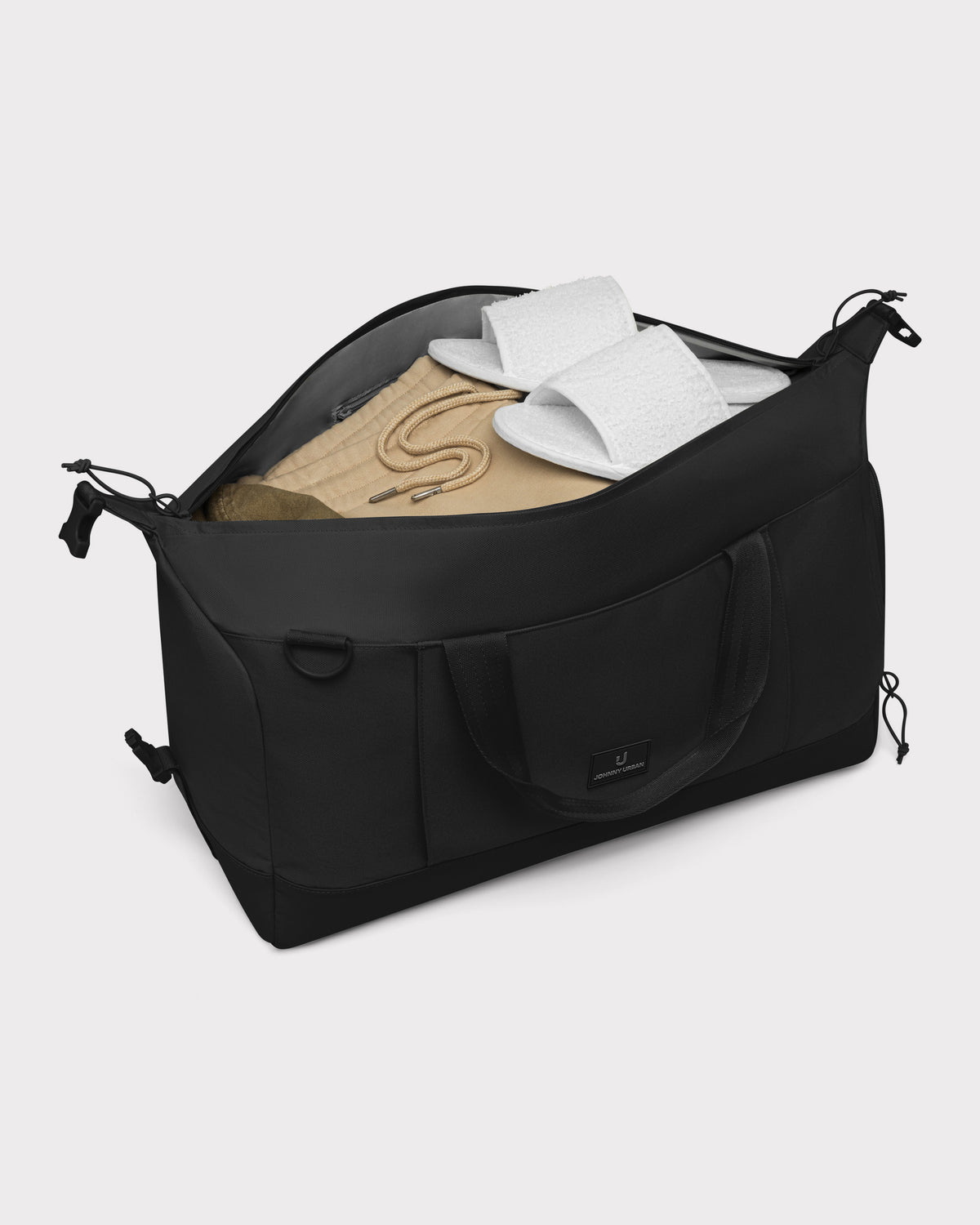 Schwarze faltbare Weekender Reisetasche 'Milan' von Johnny Urban mit beiger Kleidung und weißen Hausschuhen