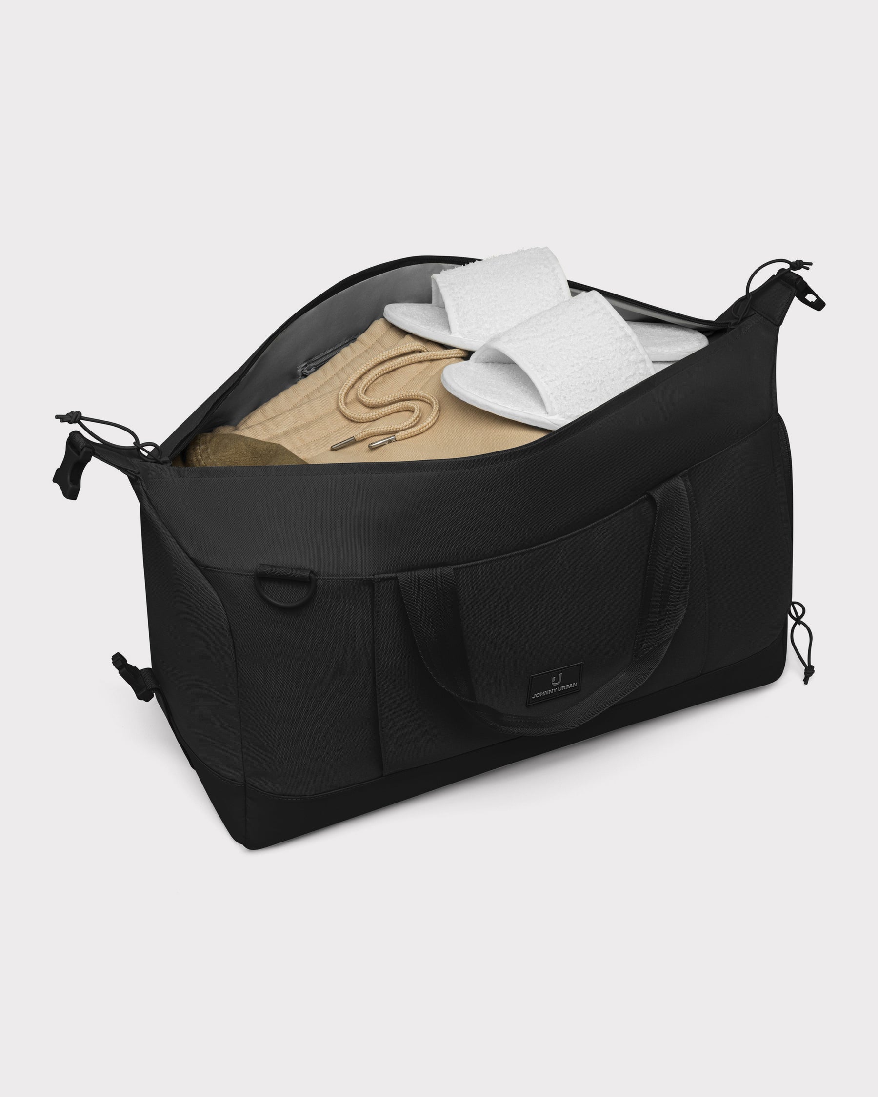Schwarze faltbare Weekender Reisetasche 'Milan' von Johnny Urban mit beiger Kleidung und weißen Hausschuhen