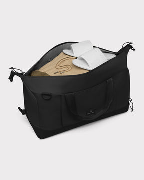 Schwarze faltbare Weekender Reisetasche 'Milan' von Johnny Urban mit beiger Kleidung und weißen Hausschuhen