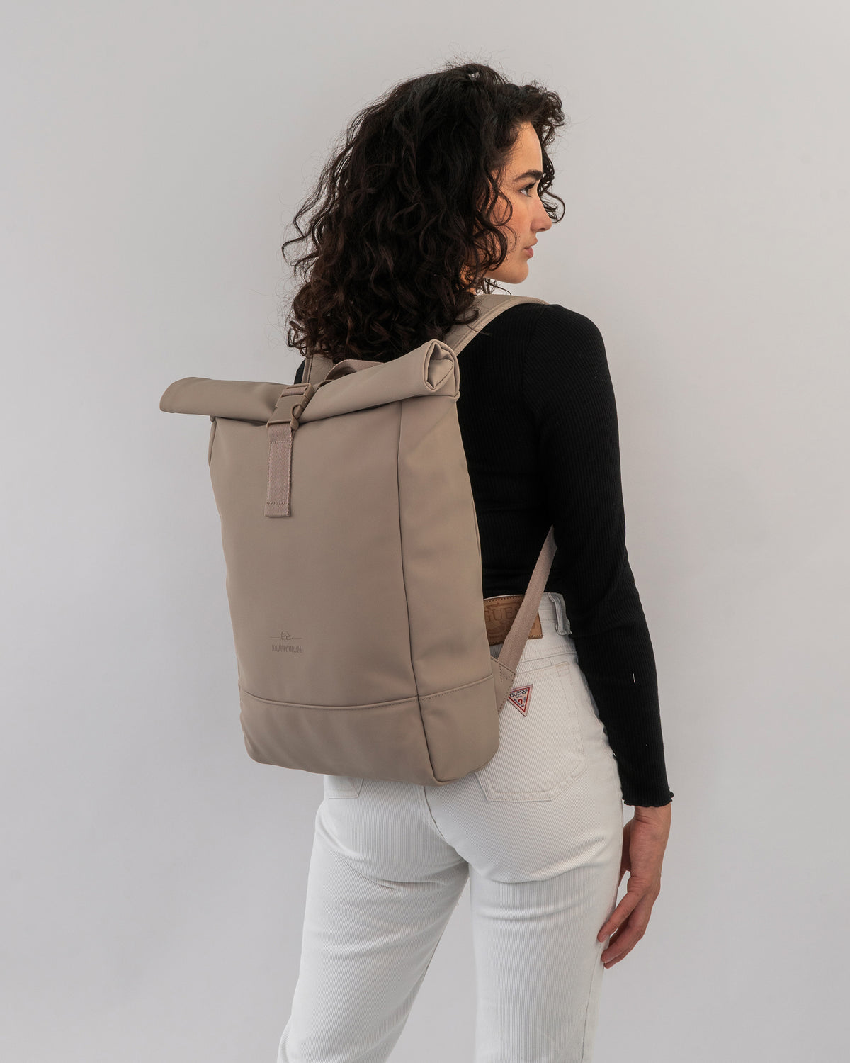 Frau mit lockigen Haaren trägt den beigen Rolltop Rucksack 'Harvey Medium' von Johnny Urban
