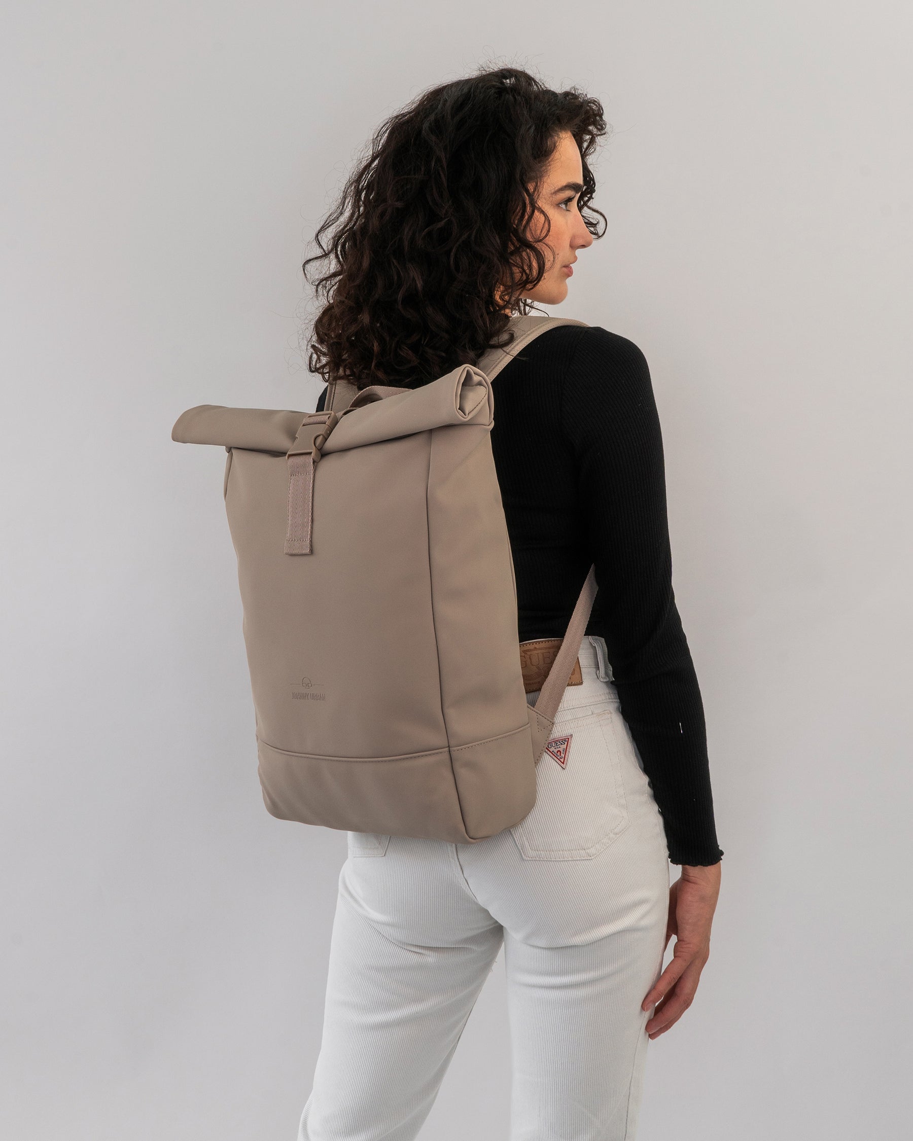 Frau mit lockigen Haaren trägt den beigen Rolltop Rucksack 'Harvey Medium' von Johnny Urban