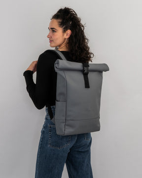 Frau trägt grauen Rolltop Rucksack 'Harvey Medium' mit schwarzem Verschluss und Trägern