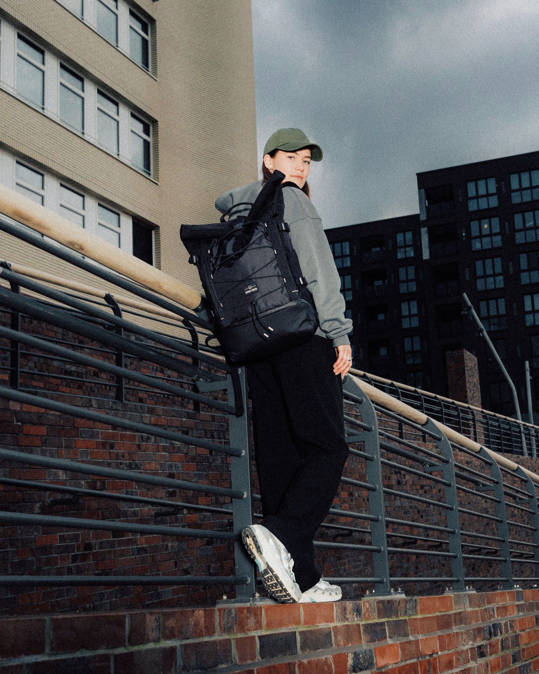 Frau mit grünem Cap trägt schwarzen Rolltop Rucksack 'Allen Large Move' urban vor Gebäuden