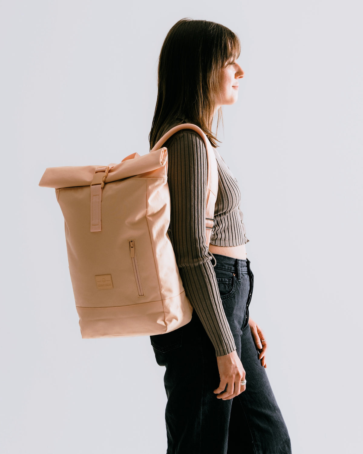 Frau trägt hellrosa Rolltop-Rucksack ‚Robin Medium‘ von Johnny Urban zu dunkler Hose und gestreiftem Oberteil