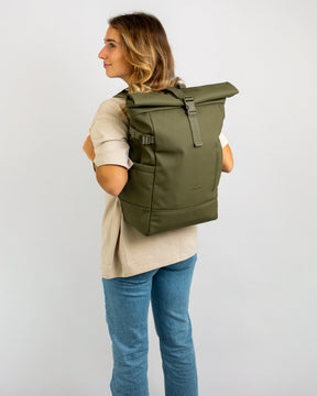 Frau mit olivgrünem Rolltop Rucksack 'Harvey Large' aus PU-Material, beige Shirt und blaue Jeans