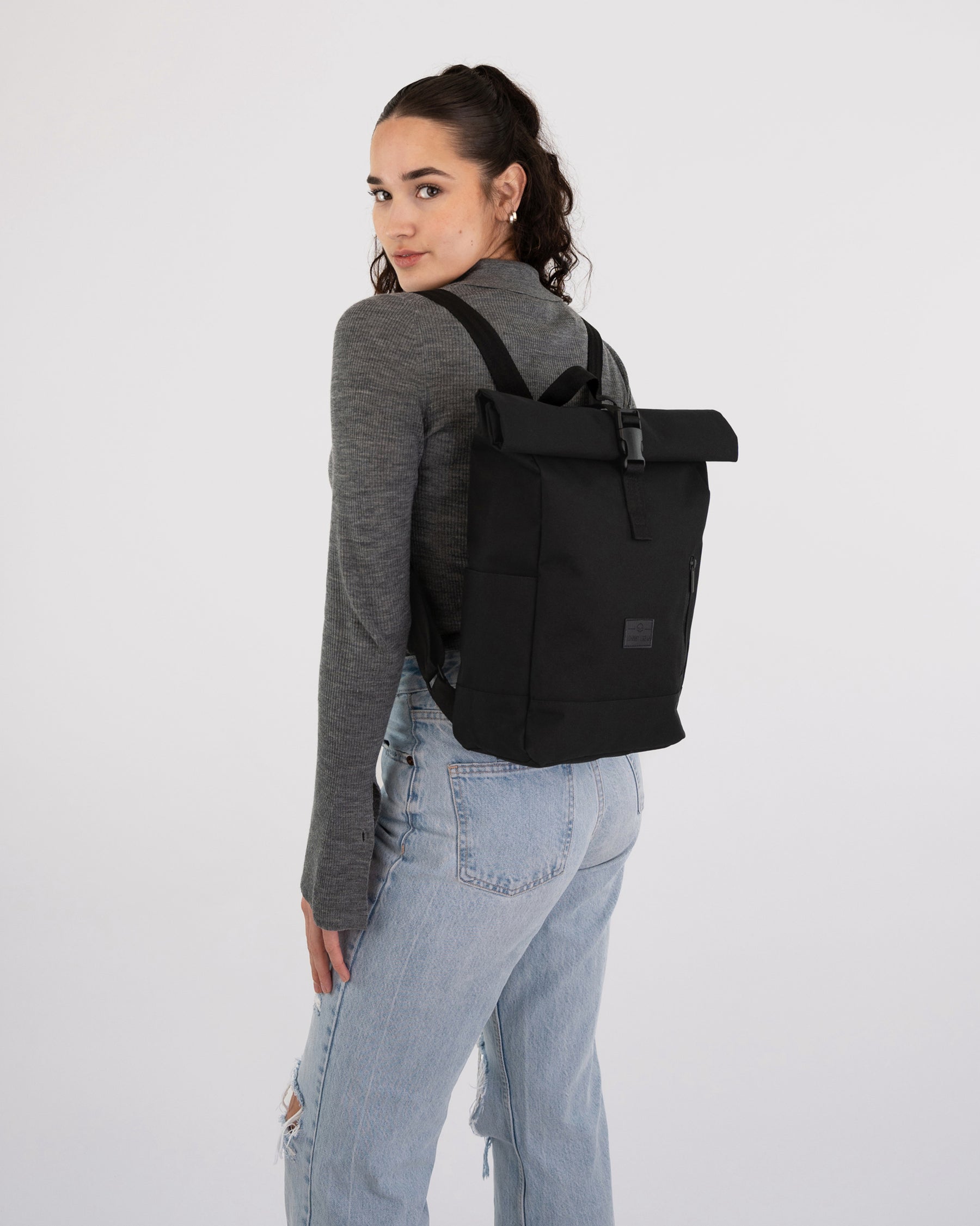 Frau mit grauem Langarmshirt und hellblauen Jeans trägt schwarzen Rolltop Rucksack 'Robin Small'