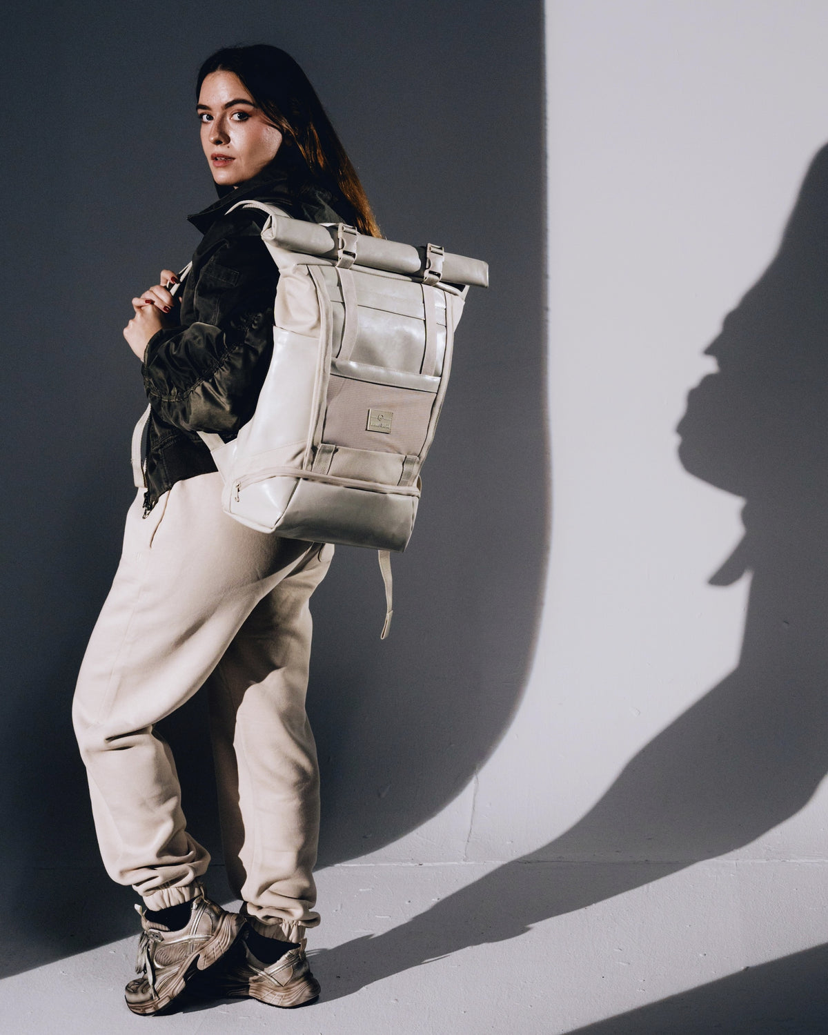 Frau trägt beigen Rolltop Rucksack 'Ashton' mit schwarzer Jacke und beigen Jogginghosen