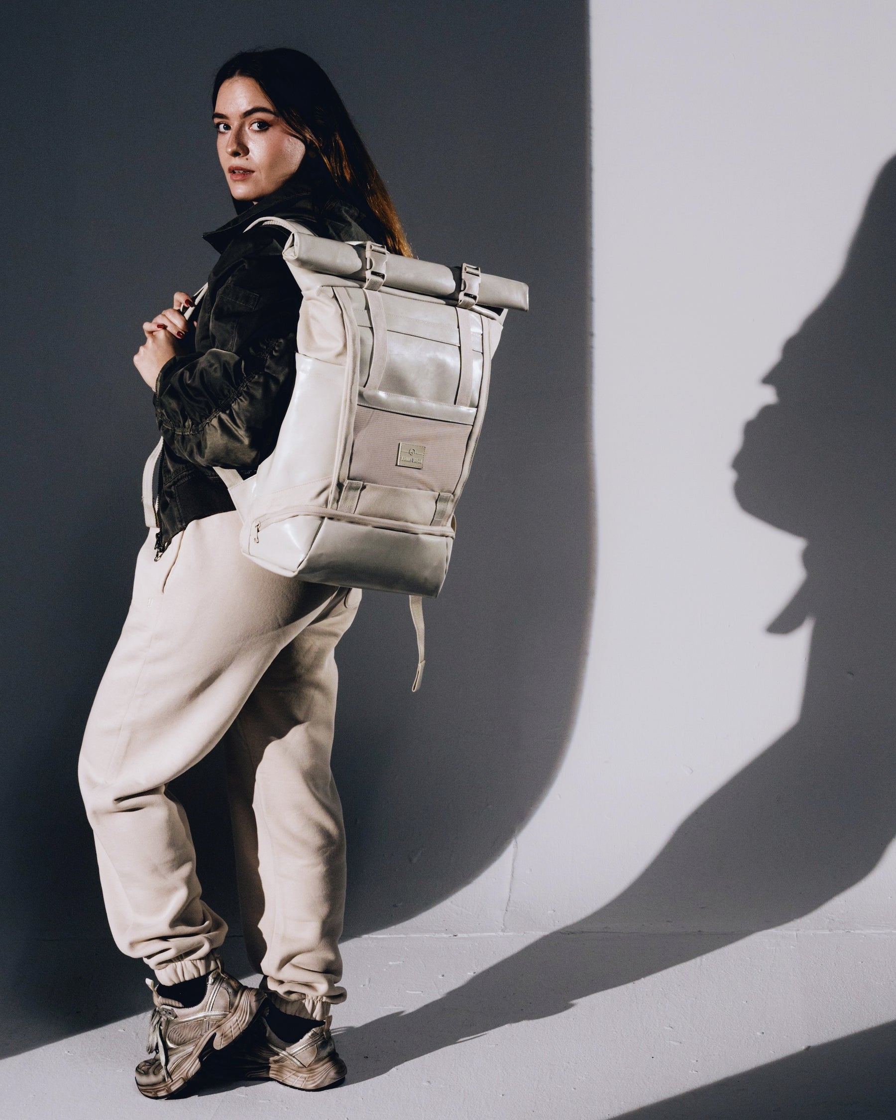 Frau trägt beigen Rolltop Rucksack 'Ashton' mit schwarzer Jacke und beigen Jogginghosen