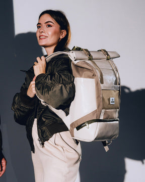 Frau trägt beigen Rolltop Rucksack 'Ashton' und schwarze Jacke