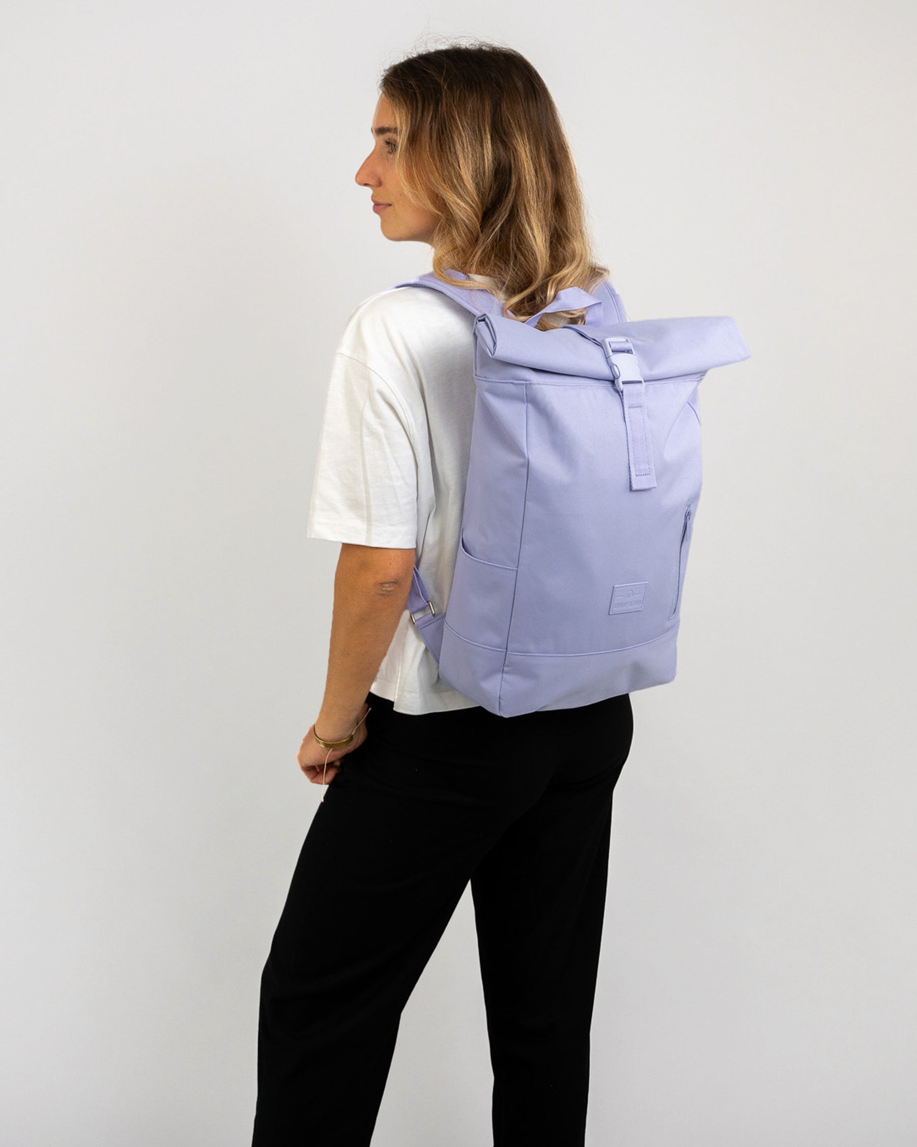 Frau mit helllila Rolltop Rucksack 'Robin Medium' von Johnny Urban, trägt weißes T-Shirt und schwarze Hose