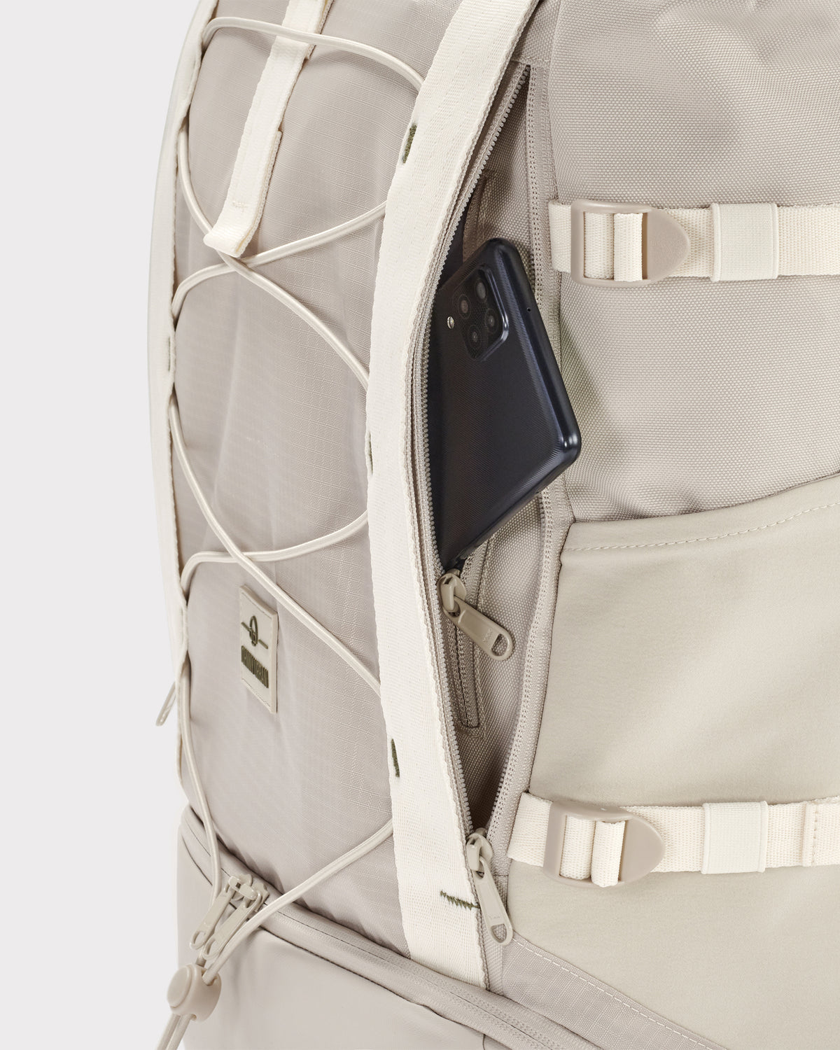 Sandfarbener Rolltop Rucksack 'Allen Large Move' mit seitlichem Geheimfach, in dem ein Smartphone steckt