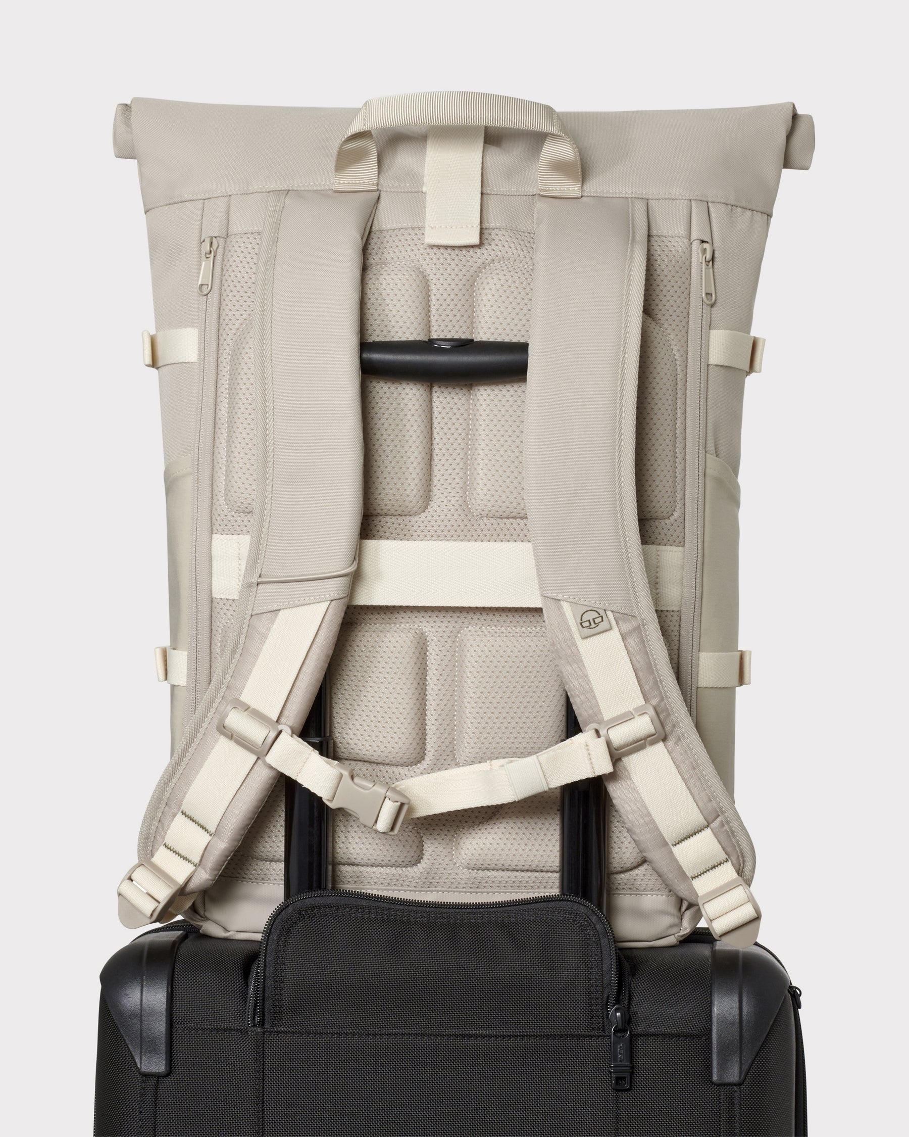 Sandfarbener Rolltop Rucksack 'Allen Large Move' mit gepolsterten Schulterriemen an einem schwarzen Koffer