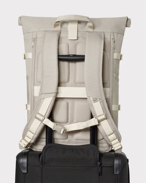 Sandfarbener Rolltop Rucksack 'Allen Large Move' mit gepolsterten Schulterriemen an einem schwarzen Koffer