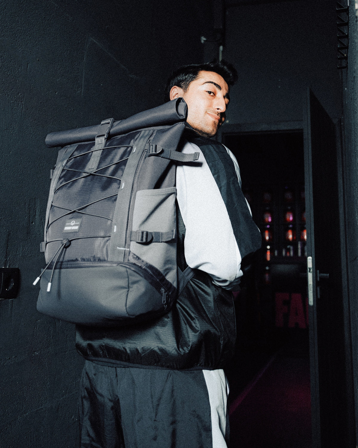 Mann trägt grauen Rolltop Rucksack 'Allen Large Move' von Johnny Urban in dunklem Flur