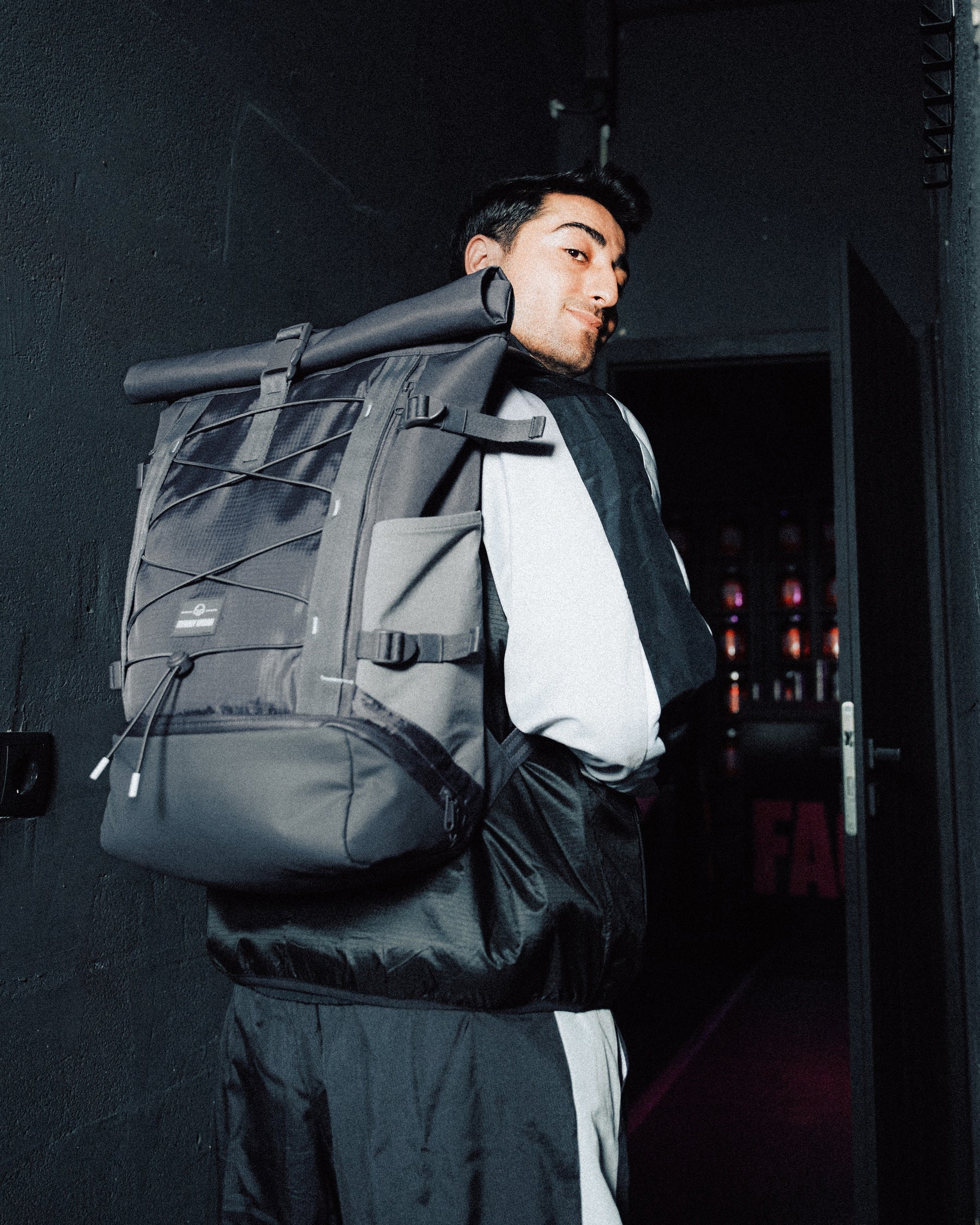 Mann trägt grauen Rolltop Rucksack 'Allen Large Move' von Johnny Urban in dunklem Flur