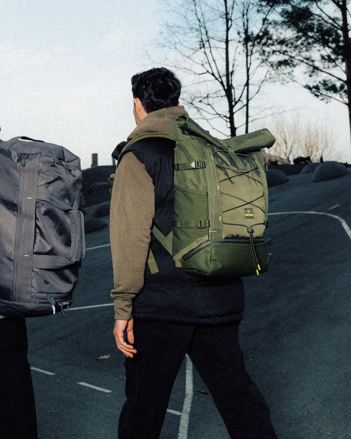Zwei Personen gehen eine Straße entlang, tragen große Rolltop-Rucksäcke in Grau und Olivgrün
