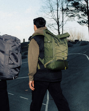 Zwei Personen gehen eine Straße entlang, tragen große Rolltop-Rucksäcke in Grau und Olivgrün