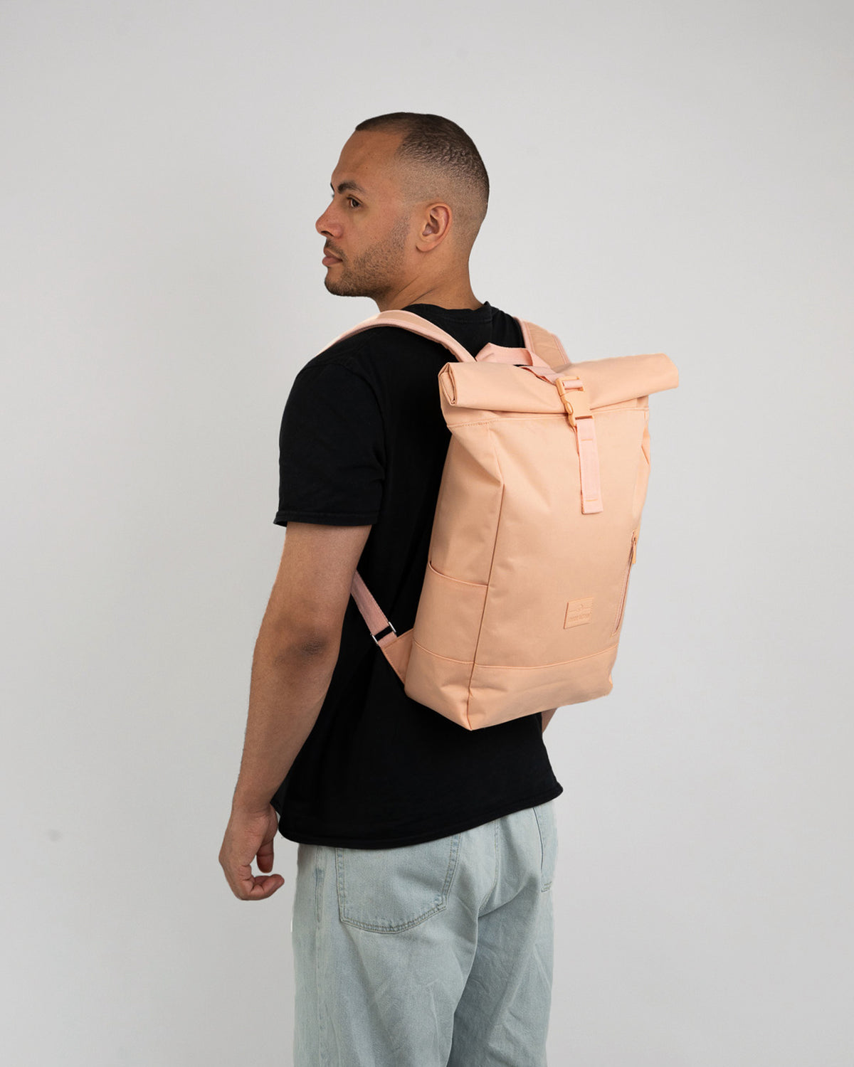 Mann von der Seite mit Johnny Urban Rolltop Rucksack 'Robin Medium' in Rosa und schwarzem T-Shirt