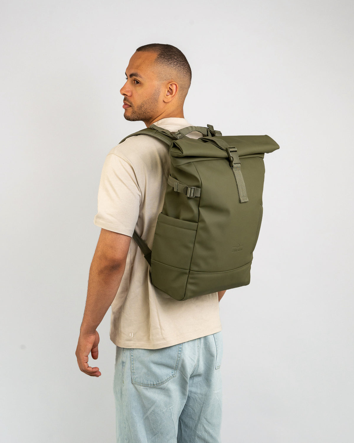 Mann trägt olivgrünen Rolltop Rucksack 'Harvey Large' von Johnny Urban, beige T-Shirt, helle Jeans