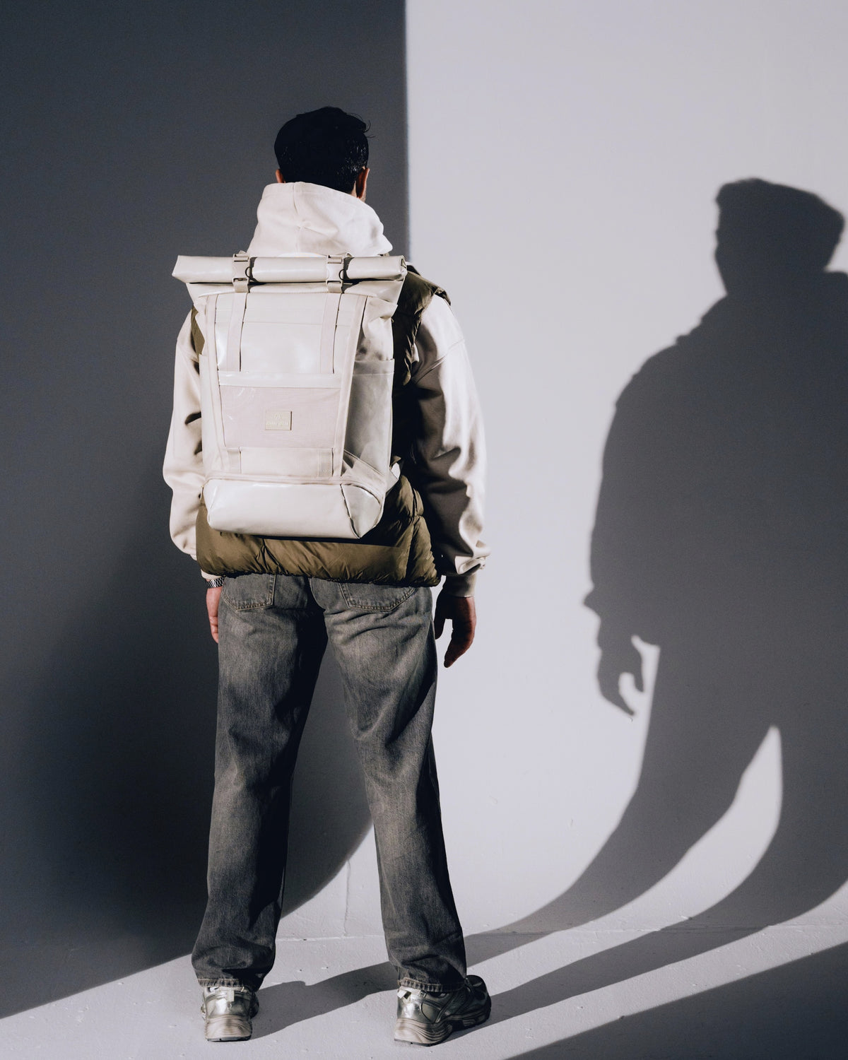 Mann von hinten mit beigefarbenem Rolltop-Rucksack 'Ashton' von Johnny Urban, trägt grüne Weste und graue Jeans
