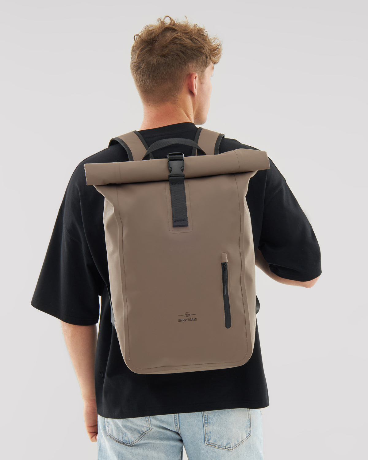 Mann von hinten mit beigem Rolltop Rucksack 'Conor' von Johnny Urban, schwarzes T-Shirt, blaue Jeans