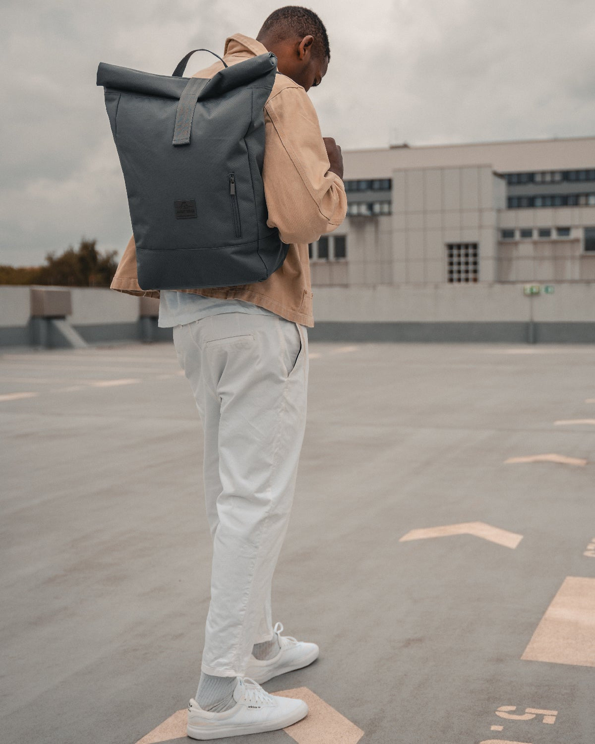Mann von hinten mit dunkelgrauem Rolltop Rucksack ‚Robin Large‘ von Johnny Urban auf einem Parkdeck