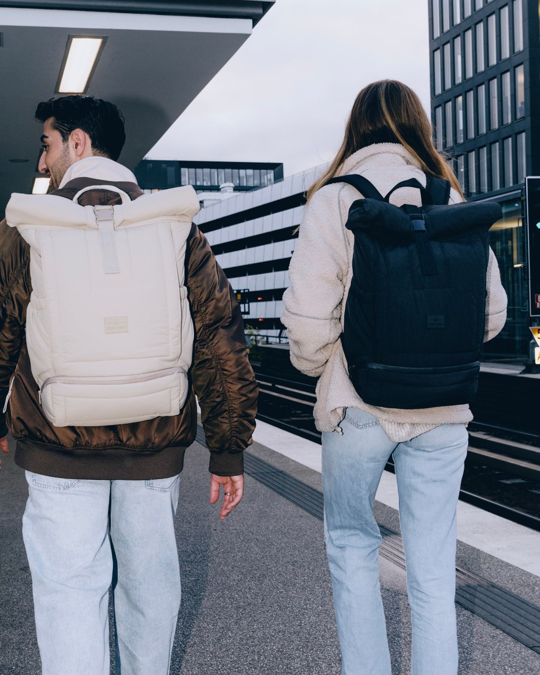 Zwei Personen in urbaner Umgebung tragen Rolltop-Rucksäcke 'Kyle' von Johnny Urban, einer hellbeige, der andere schwarz