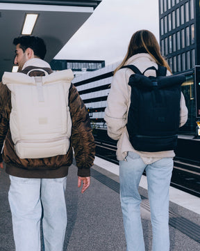 Zwei Personen in urbaner Umgebung tragen Rolltop-Rucksäcke 'Kyle' von Johnny Urban, einer hellbeige, der andere schwarz