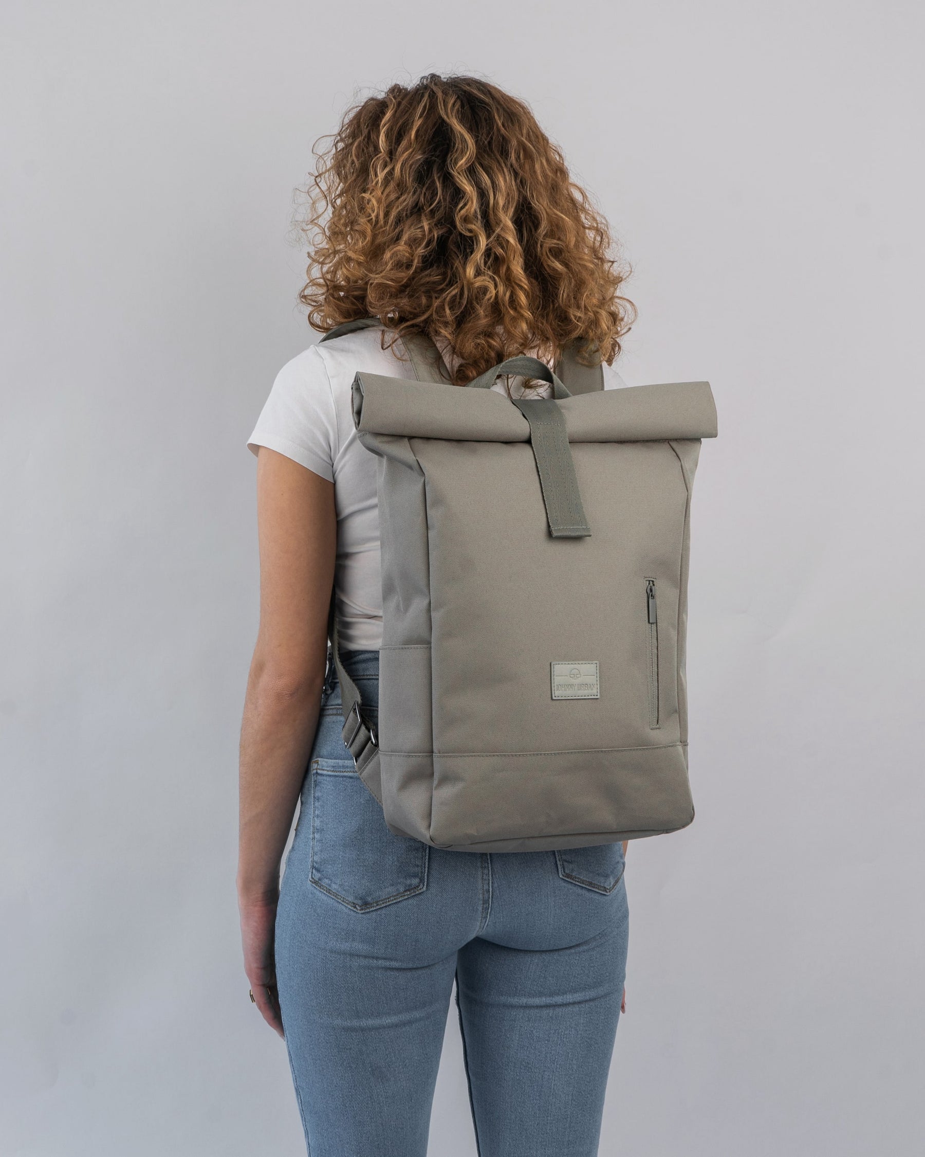 Frau mit lockigem Haar trägt den Johnny Urban Rolltop Rucksack 'Robin Medium' in desert-grey, Rückenansicht