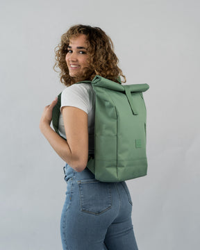 Frau trägt grünen Rolltop-Rucksack 'Robin Medium' von Johnny Urban, weißes T-Shirt, blaue Jeans