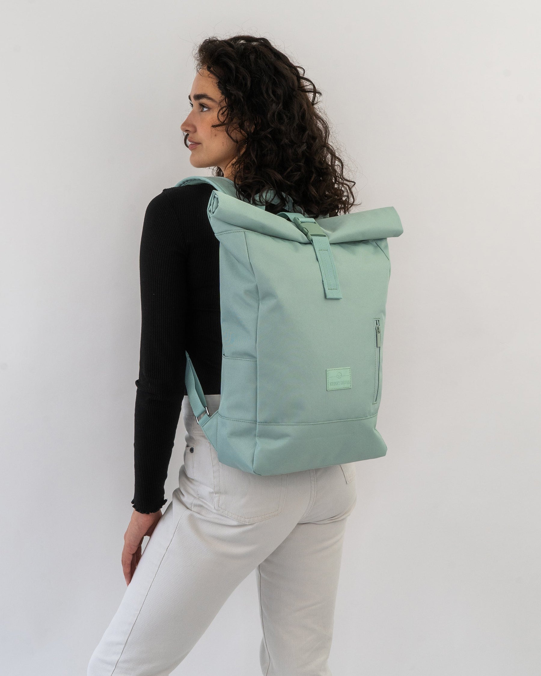 Frau mit lockigen Haaren trägt hellgrünen Rolltop-Rucksack ‚Robin Medium‘ von Johnny Urban