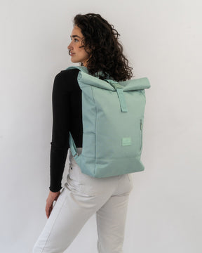 Frau mit lockigen Haaren trägt hellgrünen Rolltop-Rucksack ‚Robin Medium‘ von Johnny Urban