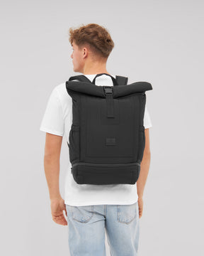 Mann mit weißem T-Shirt und Hellblauen Jeans trägt schwarzen Rolltop Rucksack 'Kyle' von Johnny Urban