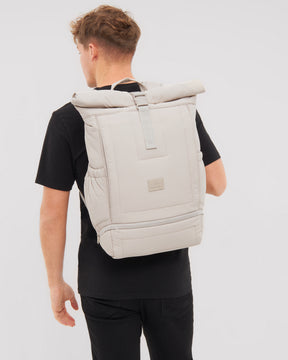 Beiger gepolsterter Rolltop-Rucksack 'Kyle' von Johnny Urban auf dem Rücken eines Mannes in schwarzem T-Shirt.