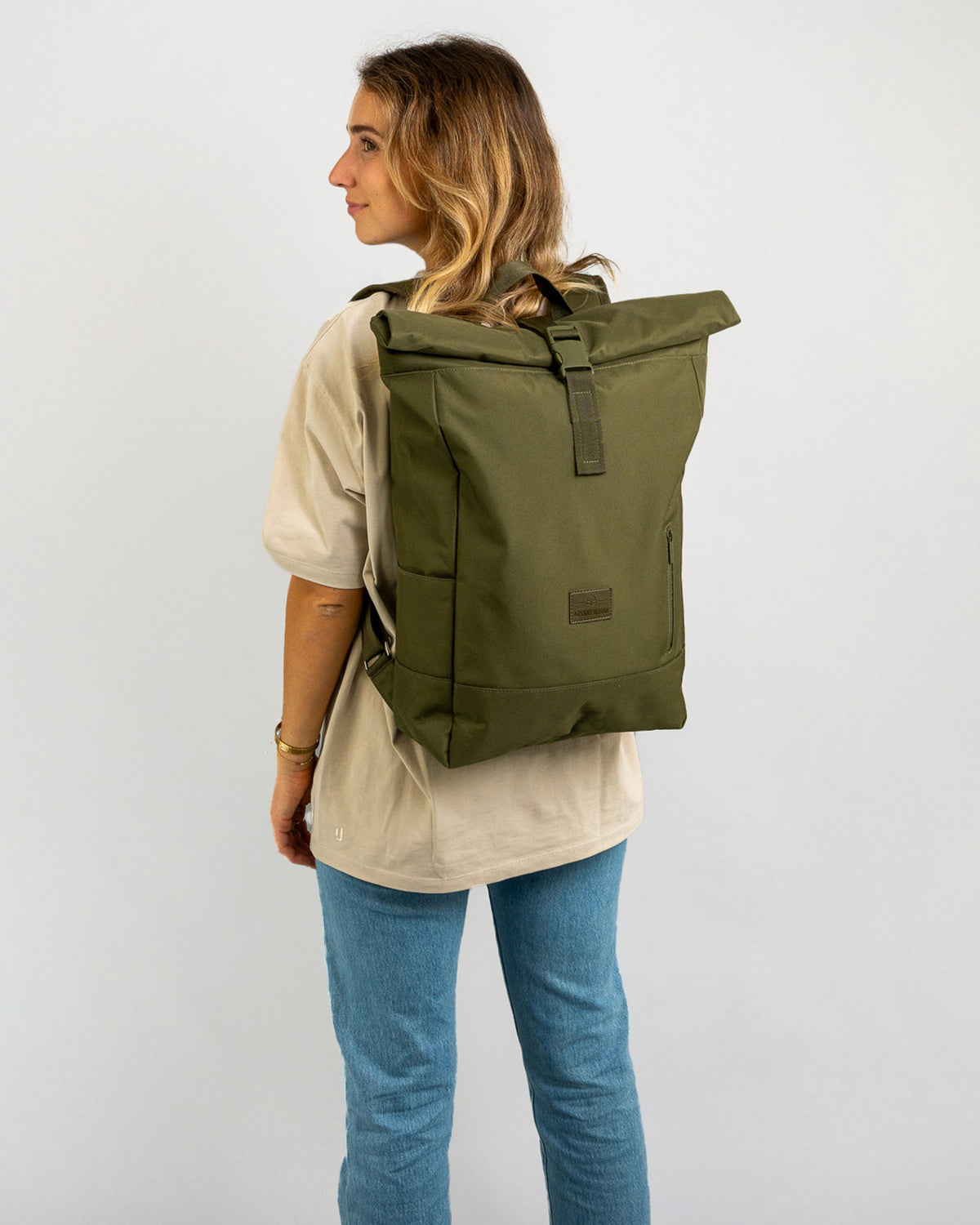 Frau trägt olivefarbenen Rolltop-Rucksack 'Robin Large' über einem beigen T-Shirt und blauen Jeans