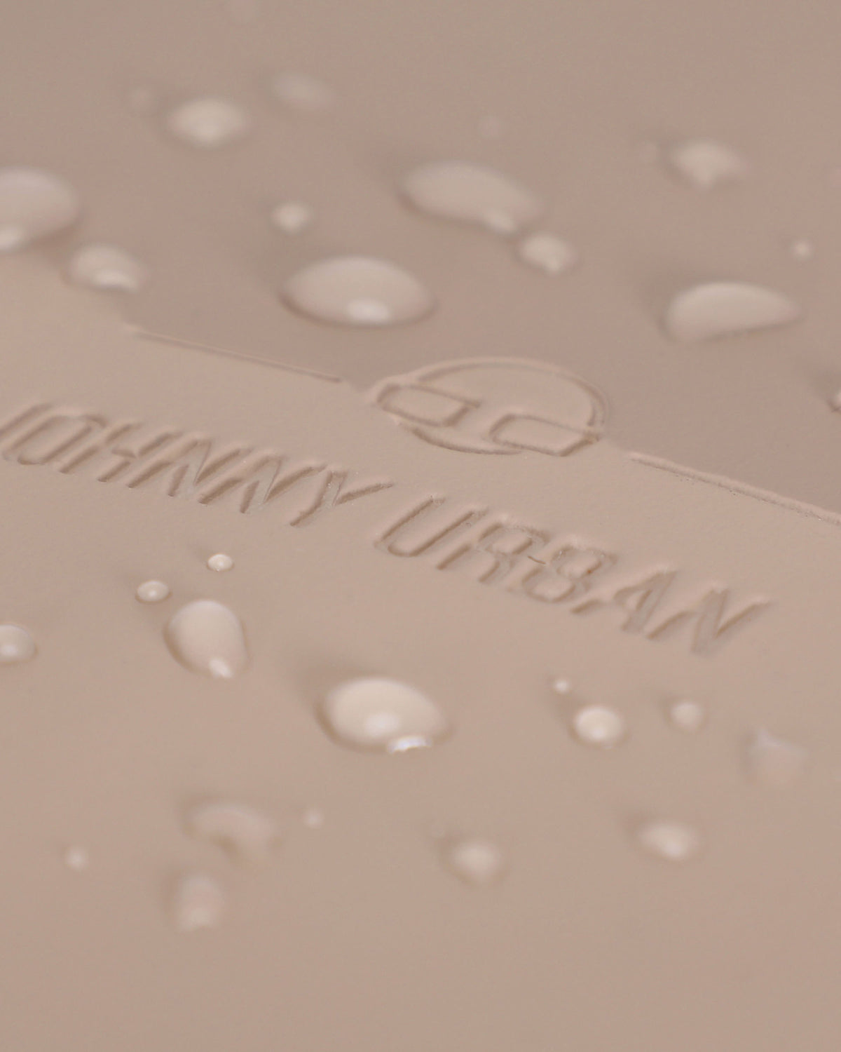 Nahe Aufnahme des beigen wasserdichten Materials mit dem eingeprägten Johnny Urban Logo und Wassertropfen