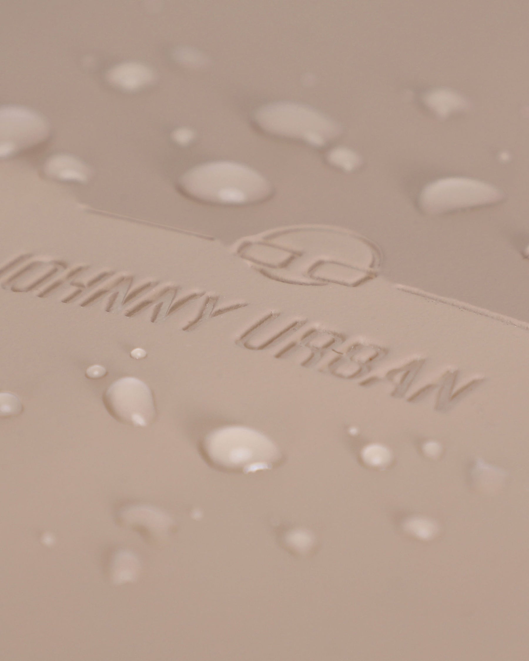 Nahe Aufnahme des beigen wasserdichten Materials mit dem eingeprägten Johnny Urban Logo und Wassertropfen