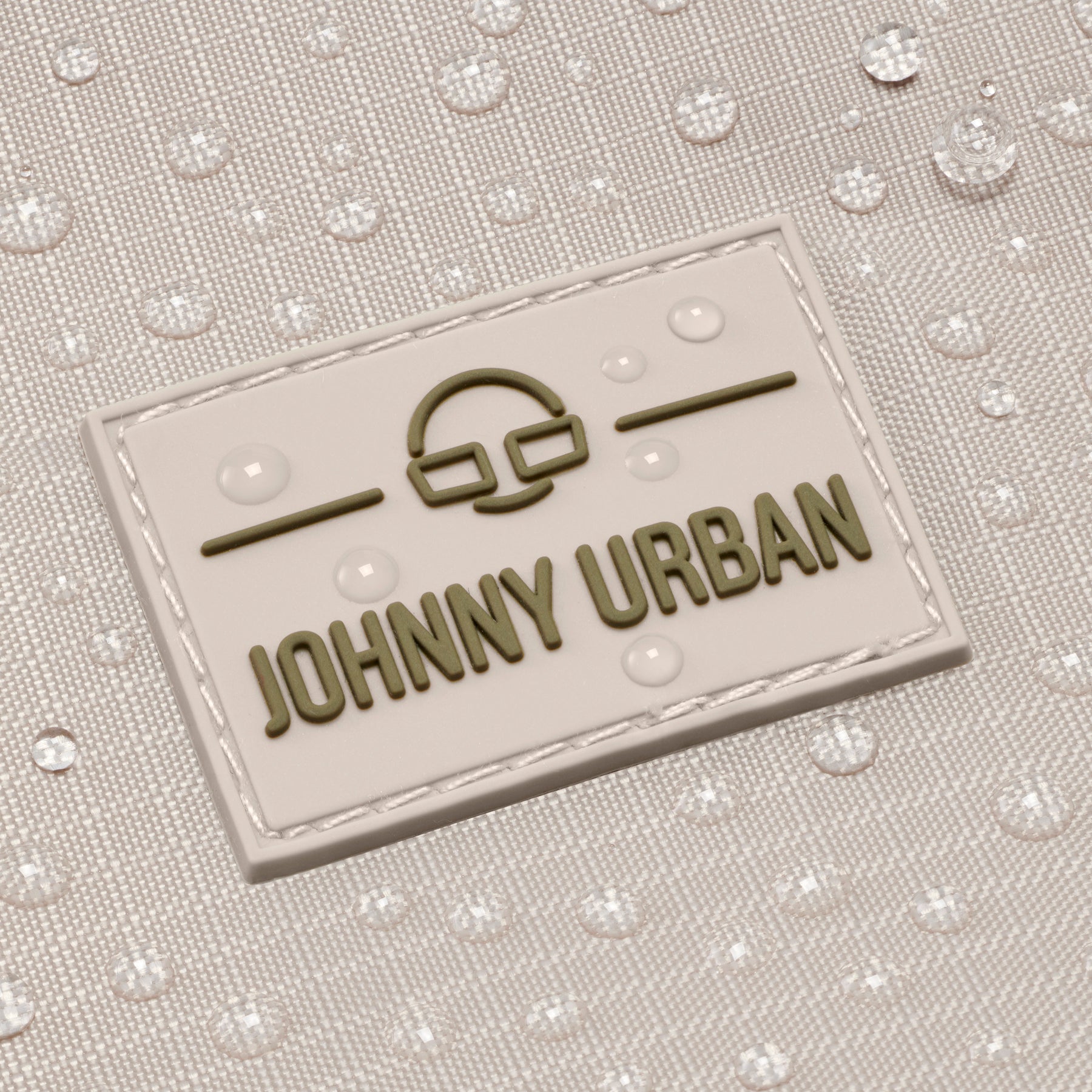 Nahe Aufnahme des wasserabweisenden sandfarbenen Johnny Urban Rolltop-Rucksacks 'Allen Large Move' mit Markenlogo und Wassertröpfchen