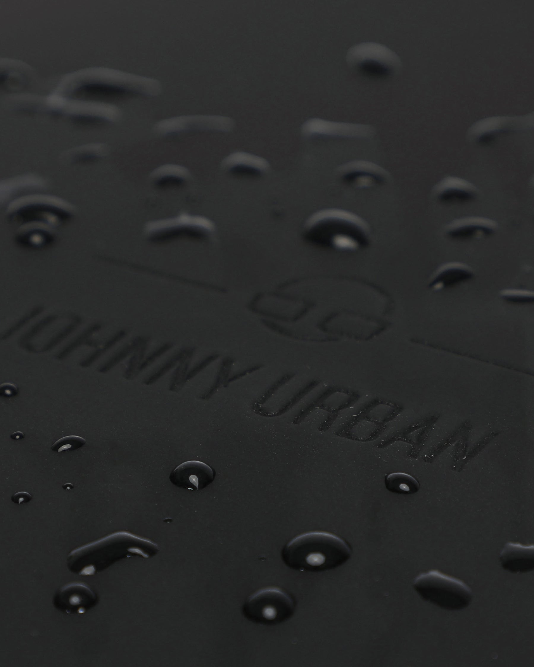 Wasserabweisende Oberfläche mit geprägtem Johnny Urban Logo auf schwarzem Material des Rolltop Rucksacks Harvey Large