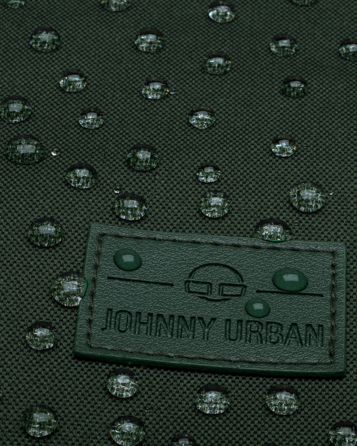 Nahaufnahme des wasserabweisenden grünen Rolltop-Rucksacks 'Robin Medium' von Johnny Urban mit Tropfen auf dem Stoff