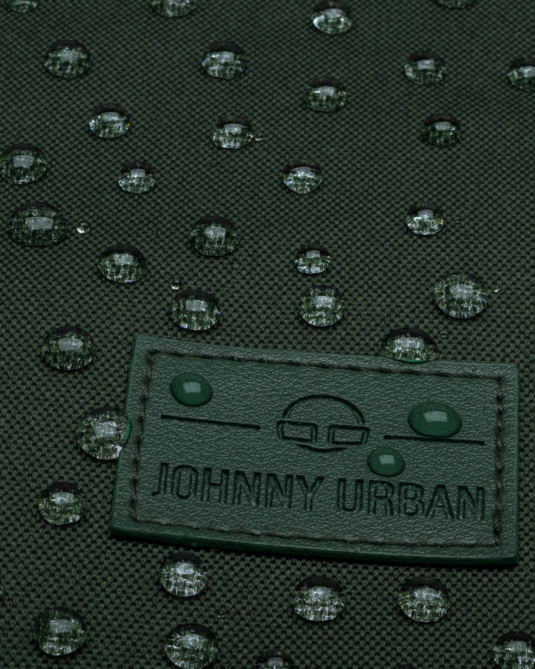 Nahaufnahme des wasserabweisenden grünen Rolltop-Rucksacks 'Robin Medium' von Johnny Urban mit Tropfen auf dem Stoff