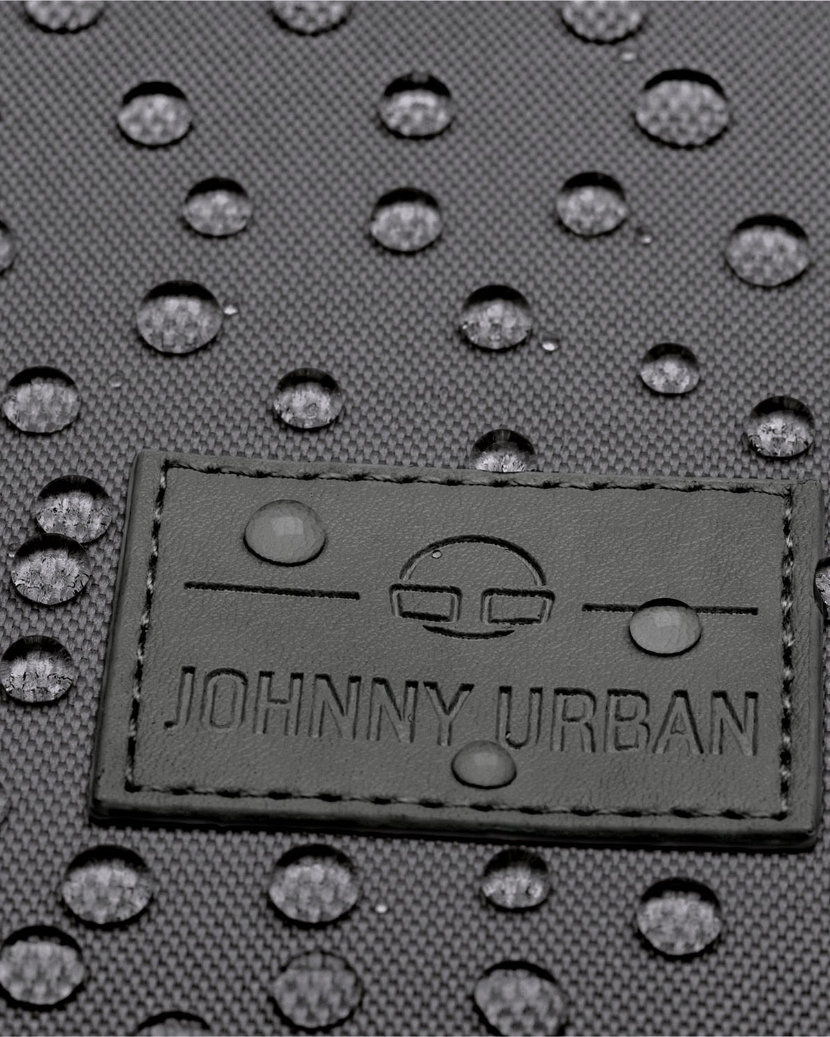 Johnny Urban Logo auf wasserabweisendem dunkelgrauem Stoff mit Wassertropfen