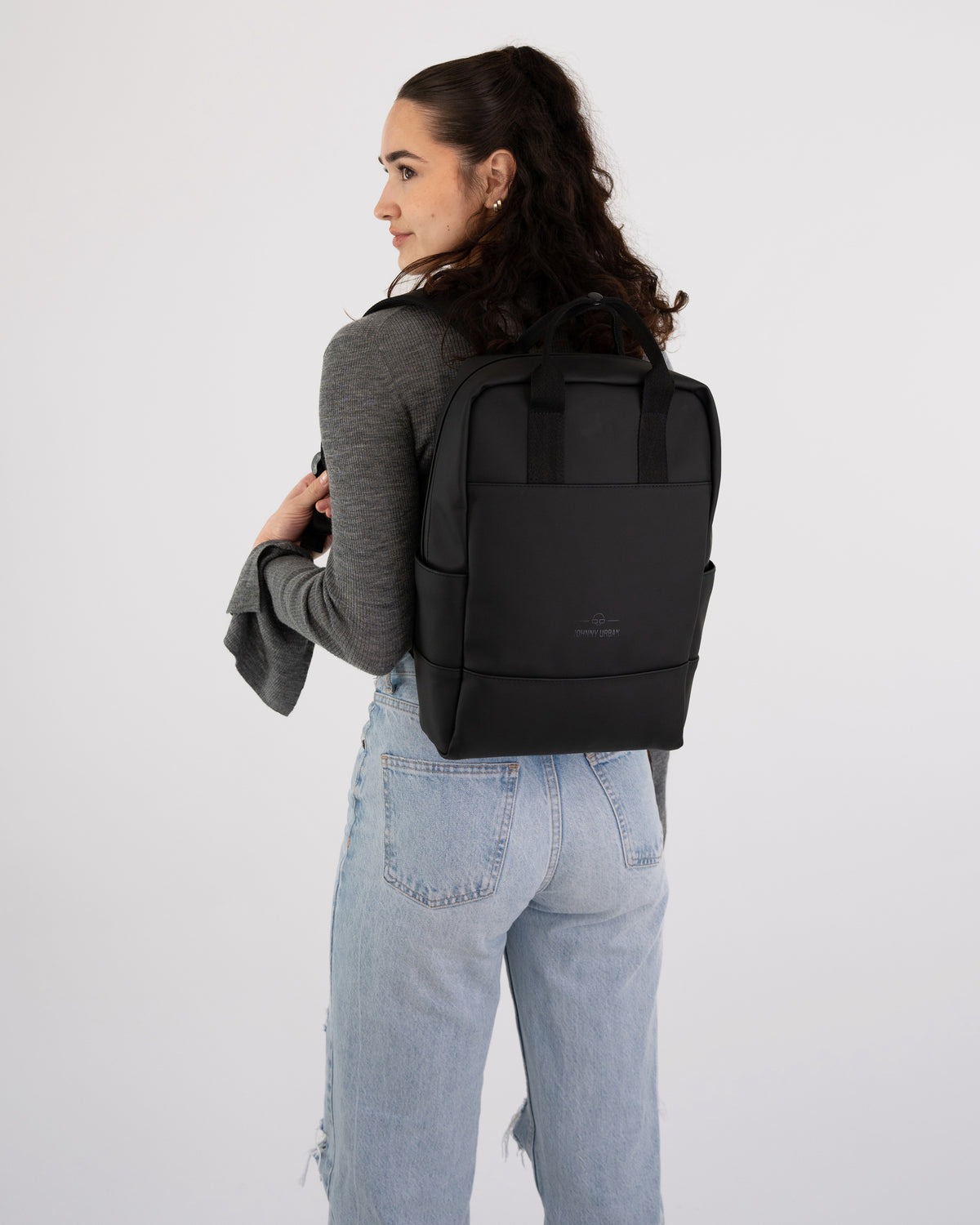 Frau mit schwarzen Rucksack 'Hailey' trägt grauen Pullover und hellblaue Jeans