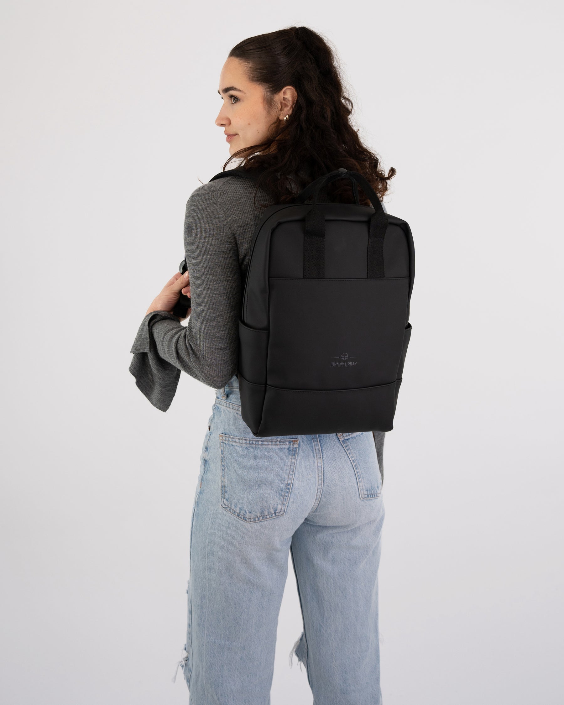Frau mit schwarzen Rucksack 'Hailey' trägt grauen Pullover und hellblaue Jeans