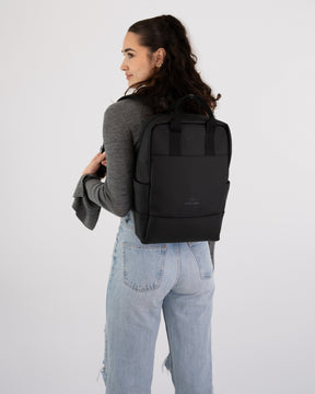 Frau mit schwarzen Rucksack 'Hailey' trägt grauen Pullover und hellblaue Jeans